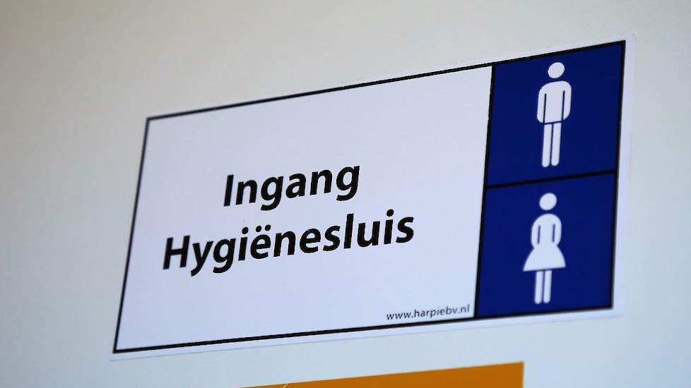 Net voor de poort is de toegang, eveneens met codeslot, tot de hygiënesluis. Bij binnenkomst in de hygiënesluis is er een kleine voorruimte en dan drie doorloopdouches met voldoende opbergruimte voor eigen kleding.